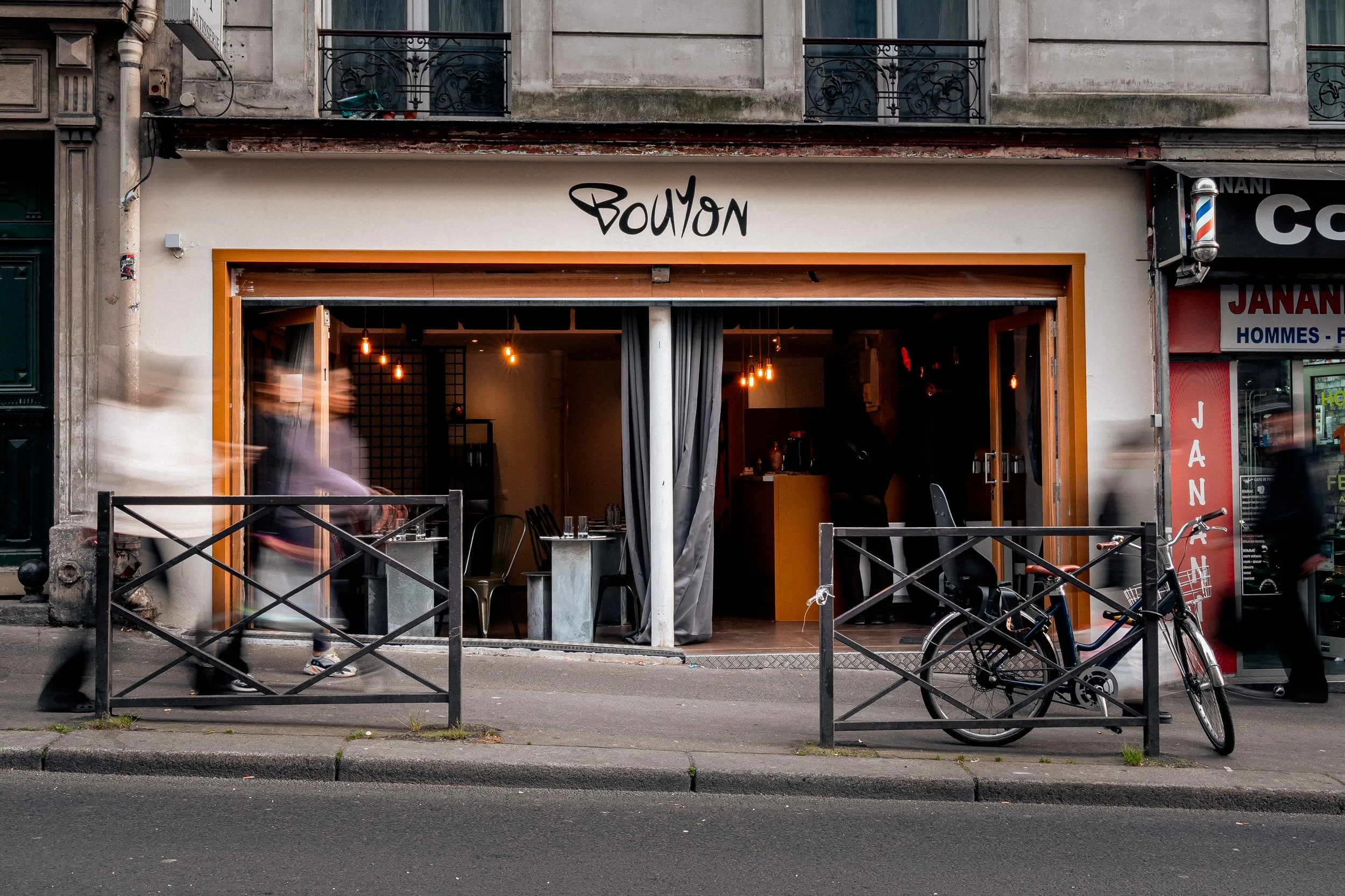 Façade du restaurant 'Bouyon' avec un intérieur visible et des gens à l'intérieur.Salle du restaurant Bouyon Belleville, afro bistro Paris 20e