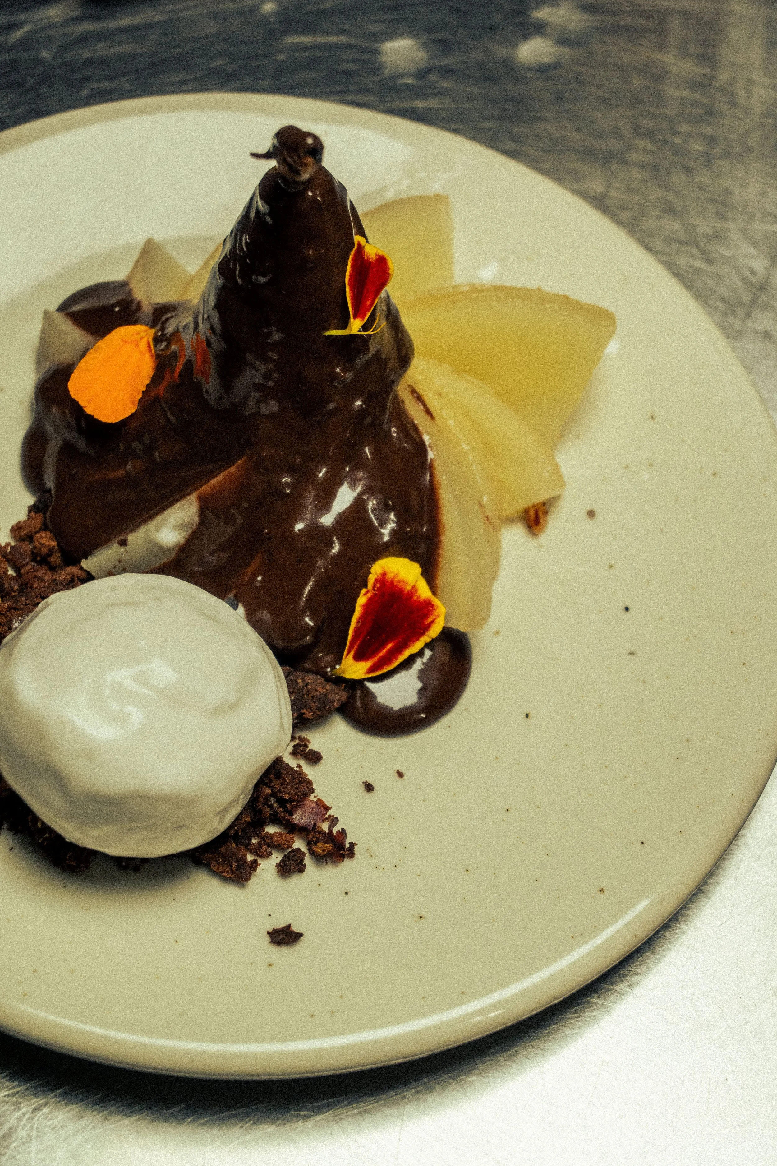 Dessert au chocolat avec une boule de glace, des tranches de poire, des fleurs comestibles et du chocolat