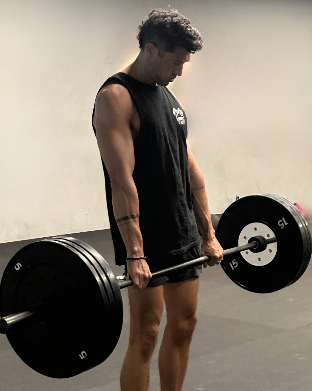 A young man with dark curly hair lifting a barbell with weights in a gym.