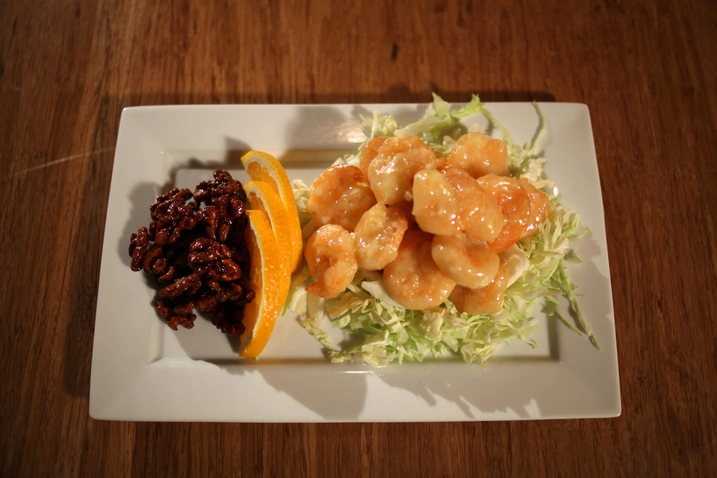 Plate of battered shrimp with orange slices, pecans, and shredded lettuce on a white rectangular plate.