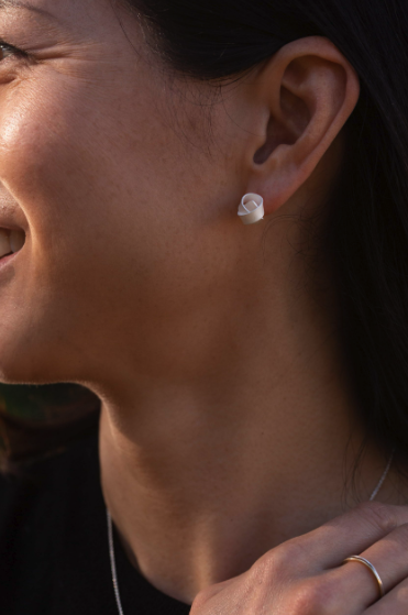 Vue partielle d'une femme montrant une boucle d'oreille blanche en forme de spirale.