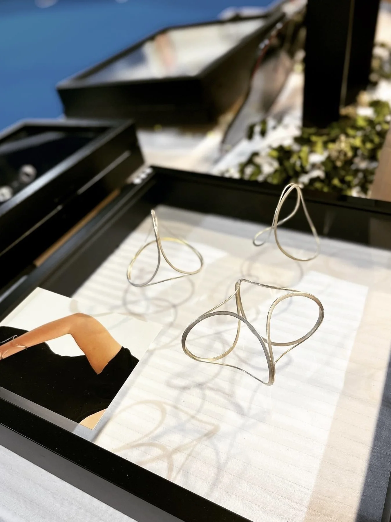 Une paire de lunettes en métal disposée sur une surface blanche, avec une photo d'une femme portant des lunettes et un grand coffret noir ouvert comportant plusieurs compartiments.
