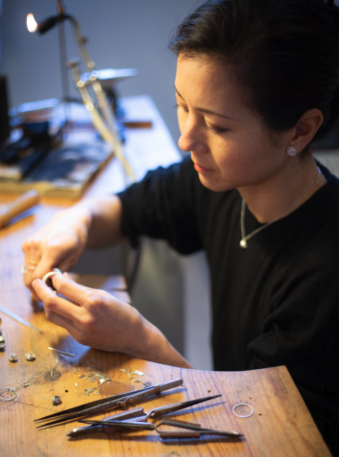 Une femme travaillant avec des outils de joaillerie sur un bureau en bois.