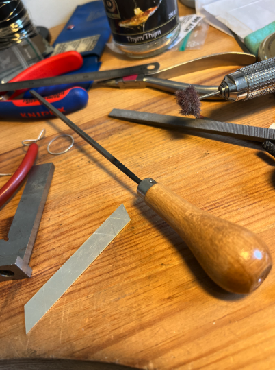 Outils de bricolage sur une table en bois, y compris un tournevis avec une poignée en bois, une lime, des pinces, et divers autres outils.