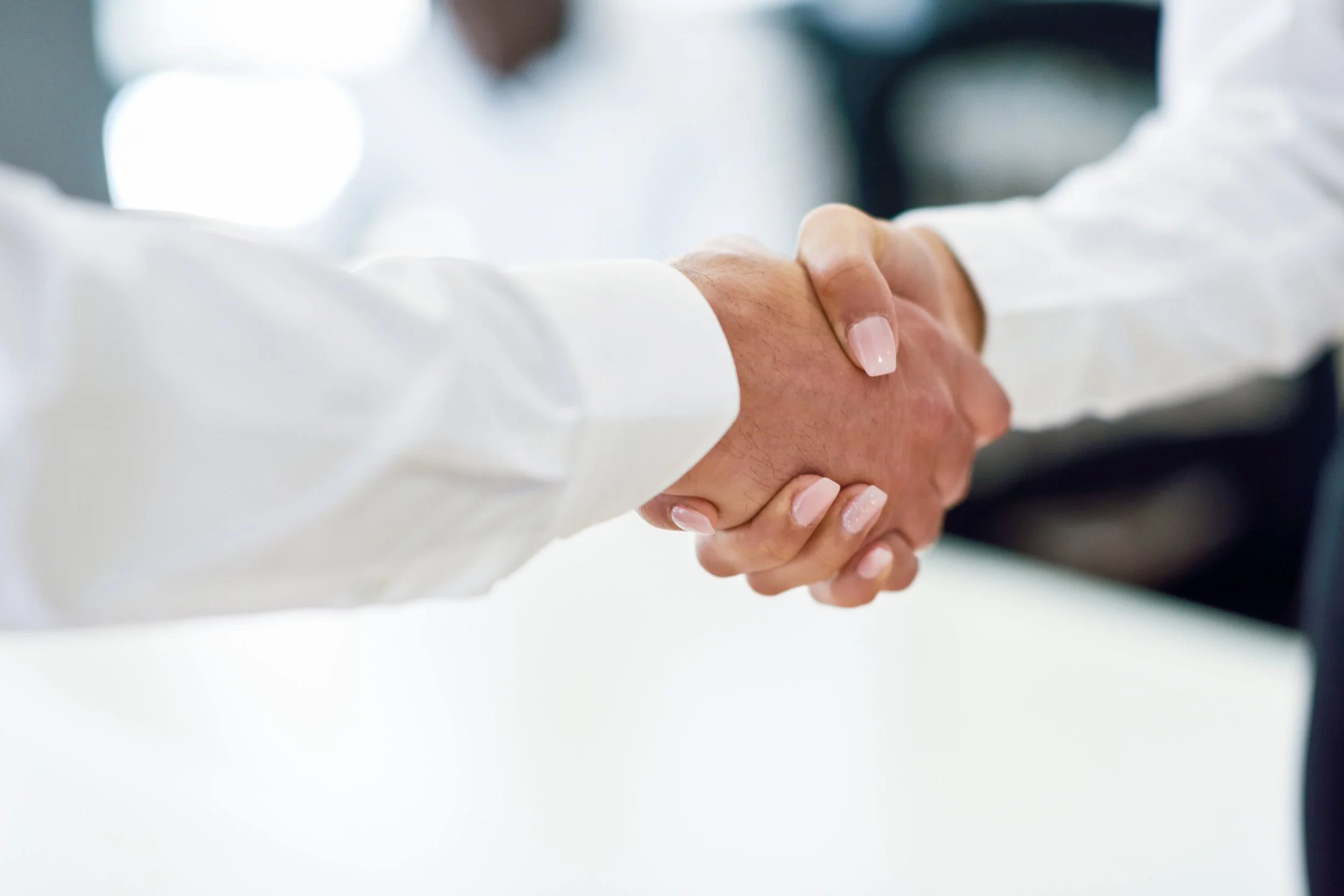 Two people shaking hands in a professional setting, with both wearing dress shirts.