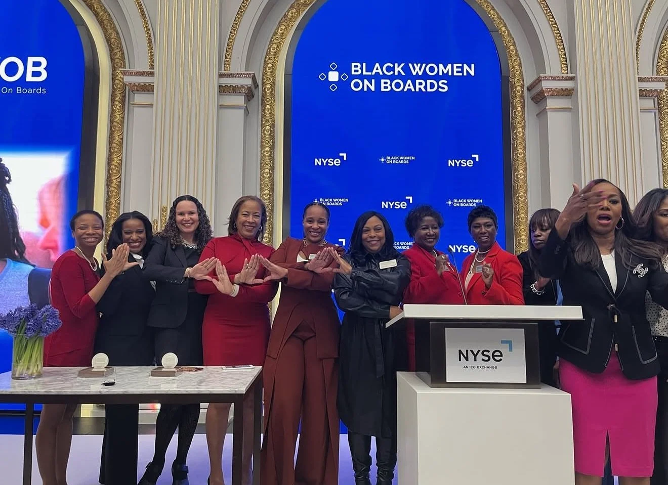 Group of women standing at the NYSE podium during an event titled 'Black Women on Boards,' with a large blue screen behind them displaying the event name and NYSE logo.