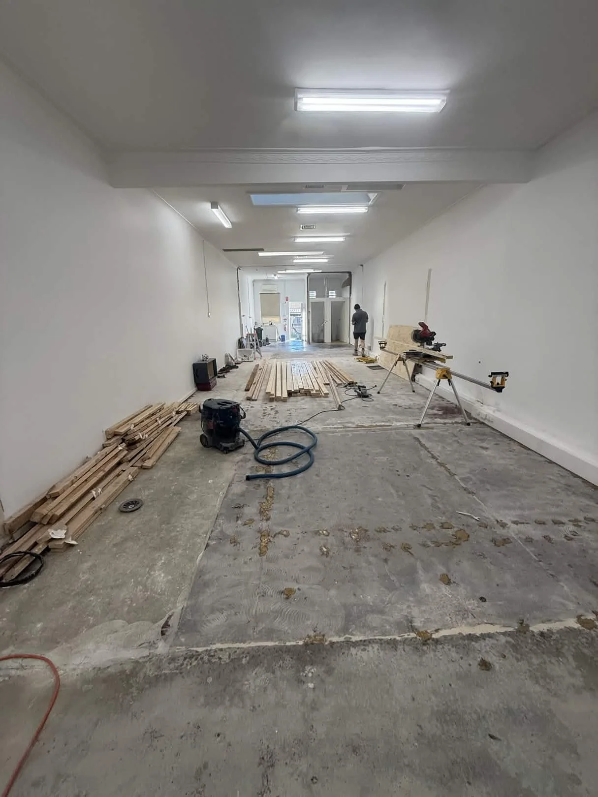 An indoor construction site with wooden planks, construction tools, and a worker in the background.