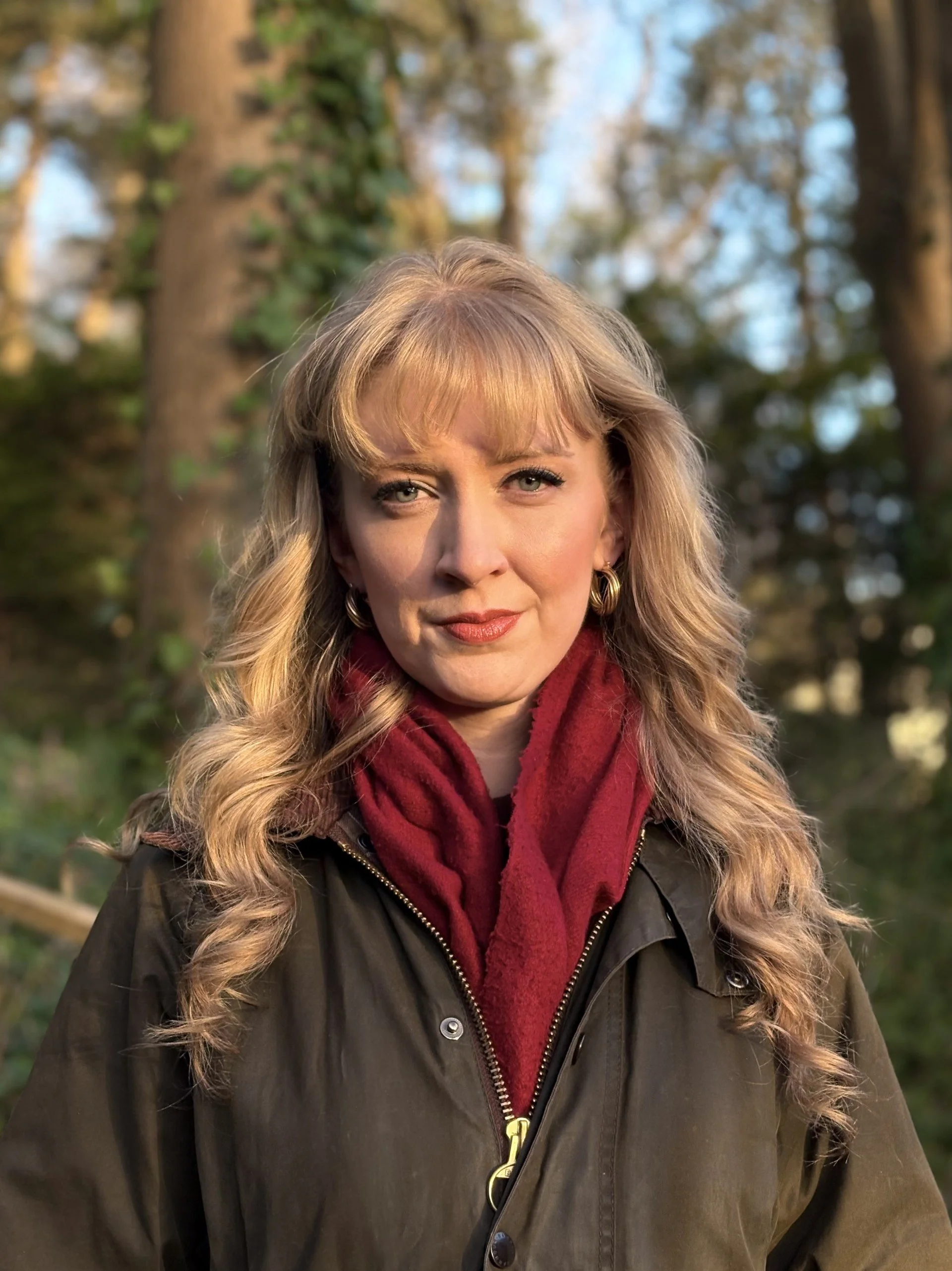 Madeleine Hall looking at the camera with a smile. She is wearing a coat and a scarf, looking like she's out on location