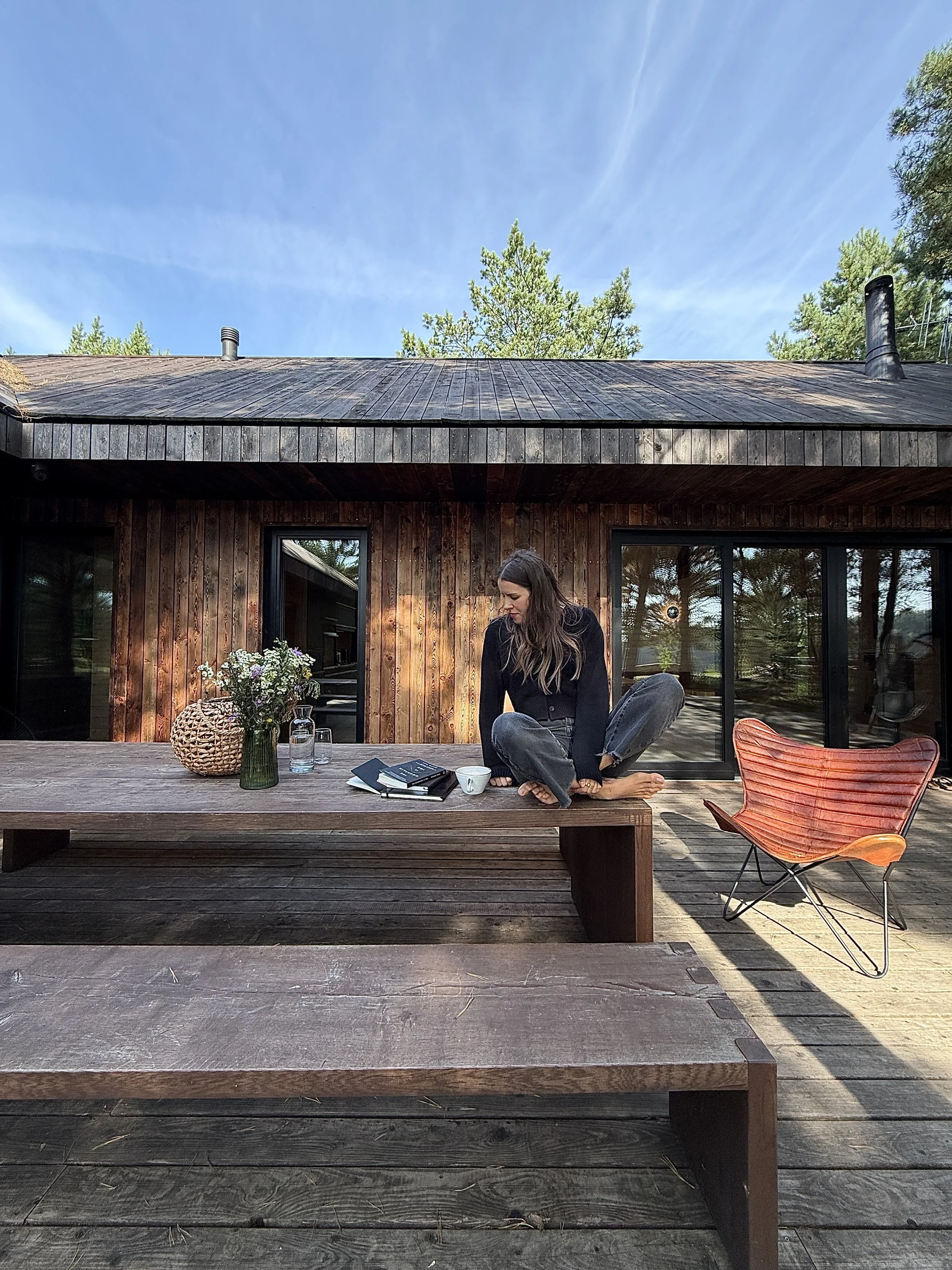 Anna Retel sitting outside a wooden cabin with a notebook on a sunny day