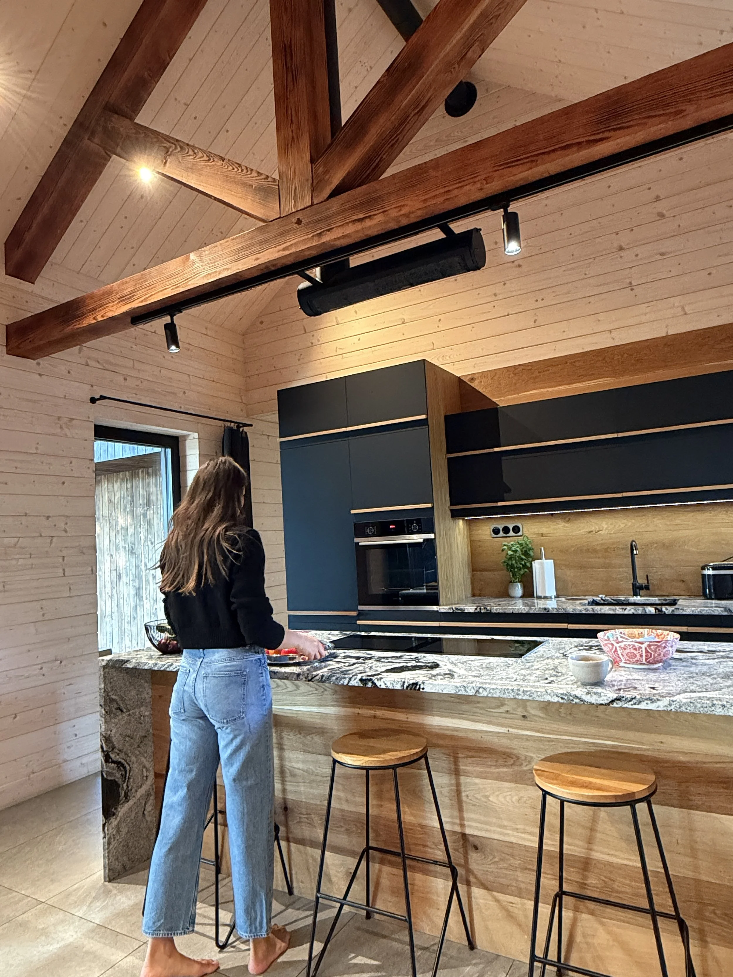Anna Retel preparing food at a kitchen counter in a modern wooden kitchen with bar stools