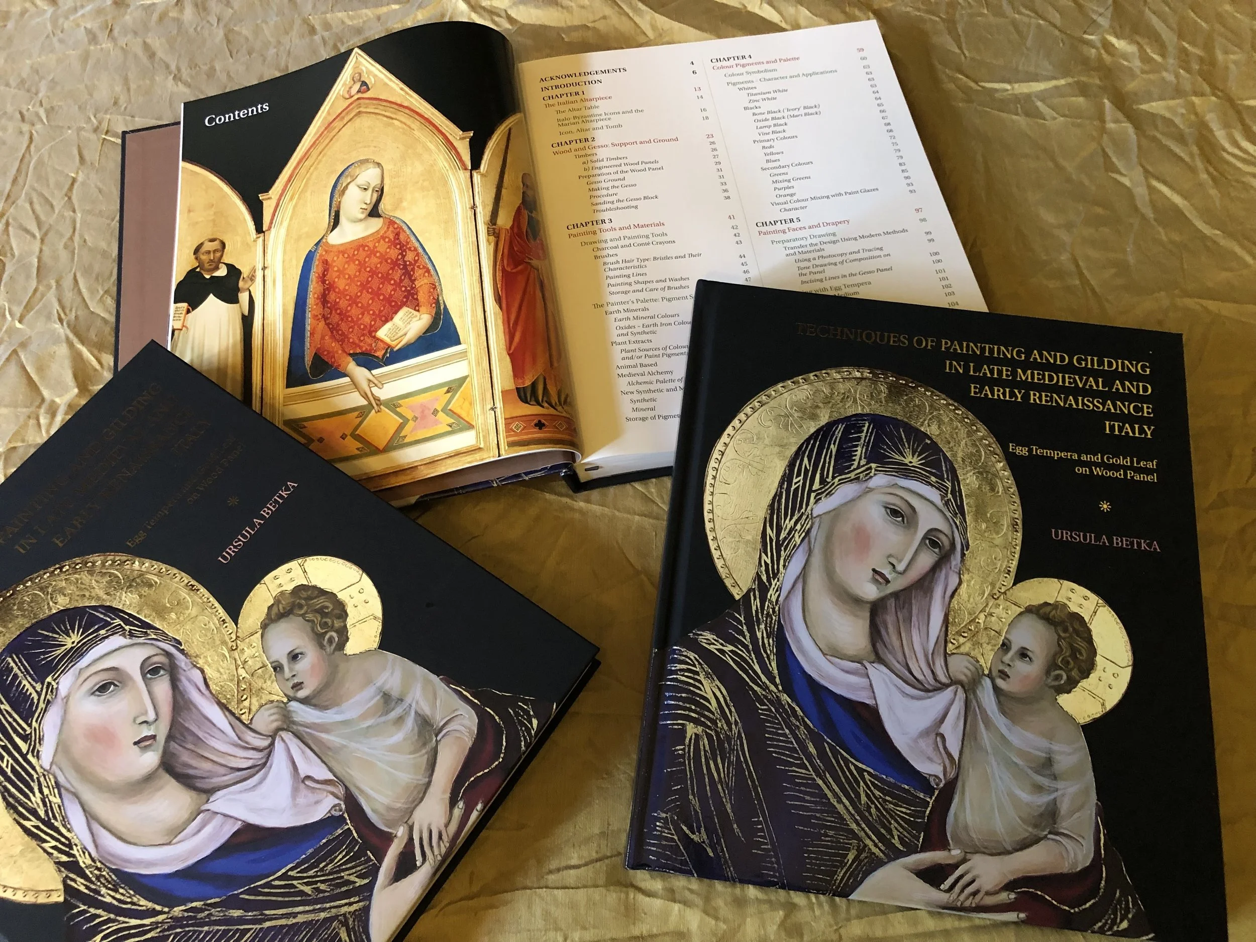 Open books on a wooden surface showing illustrations of religious figures, including a Madonna and Child with gold halos.