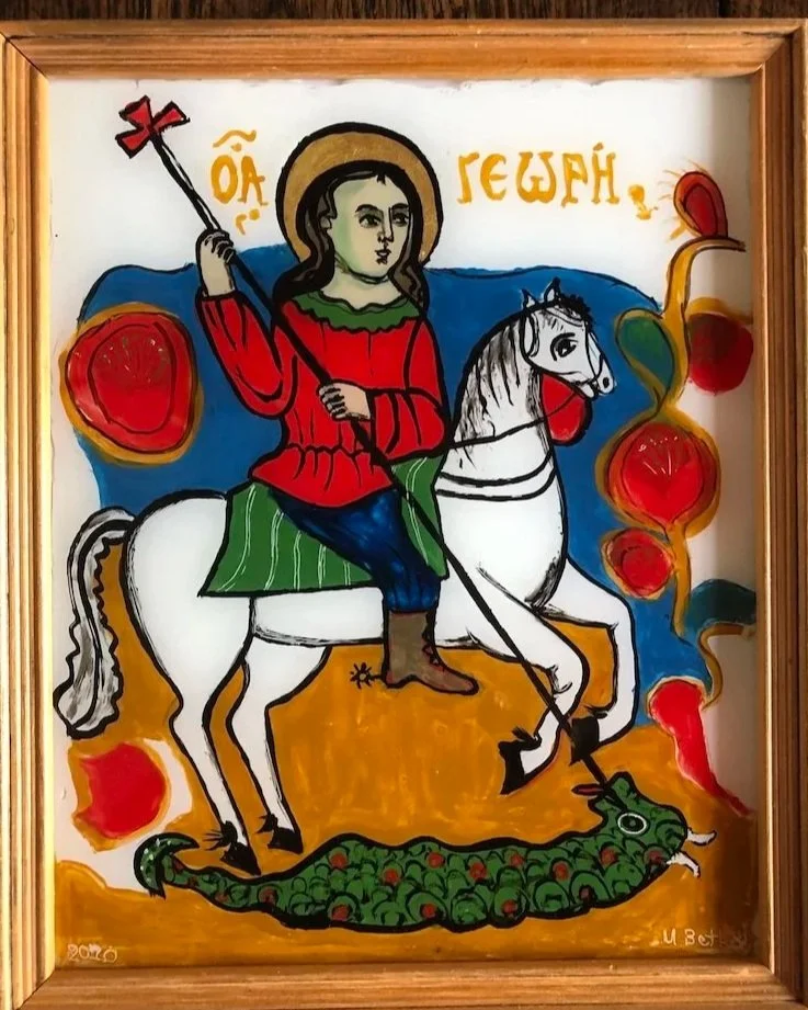 Colorful painting of Saint George on a white horse, wearing a red shirt and green cloak, holding a spear. The horse is standing on a green serpent with red eyes, and the background features abstract red and yellow shapes. There is text in a language that appears to be Cyrillic at the top of the painting.