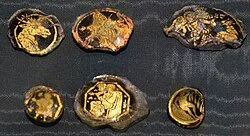 Seven gold nuggets of various sizes on a dark surface.