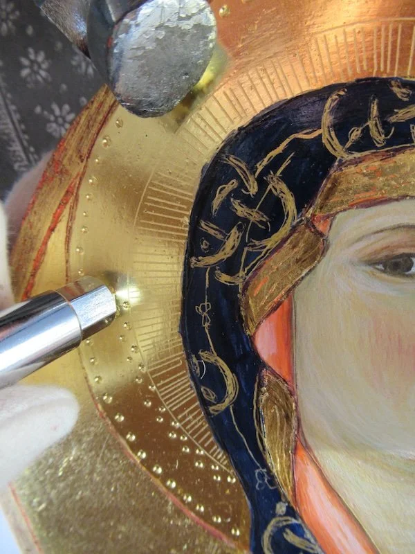 Close-up of a religious icon painting featuring a partially visible face of a woman with a gilded halo and intricate dark blue and gold head covering.