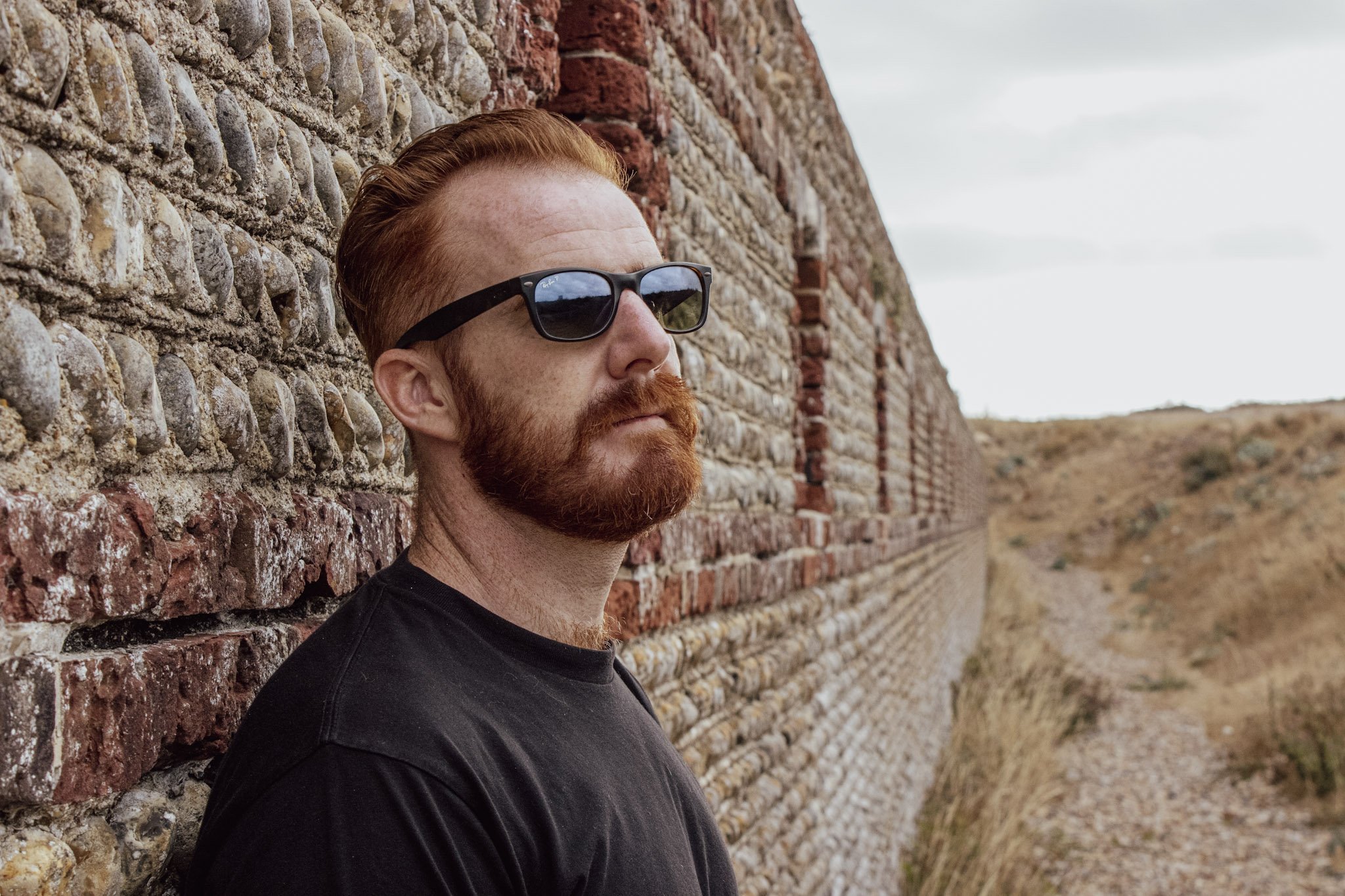 Cam Springett in sunglasses, leaning against an old brick and flint wall
