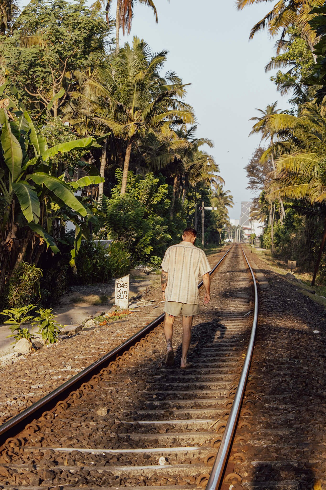 Cam Springett, online sobriety and performance coach, walking along a railway track in Ahangama, Sri Lanka, back to camera, wearing a linen shirt.