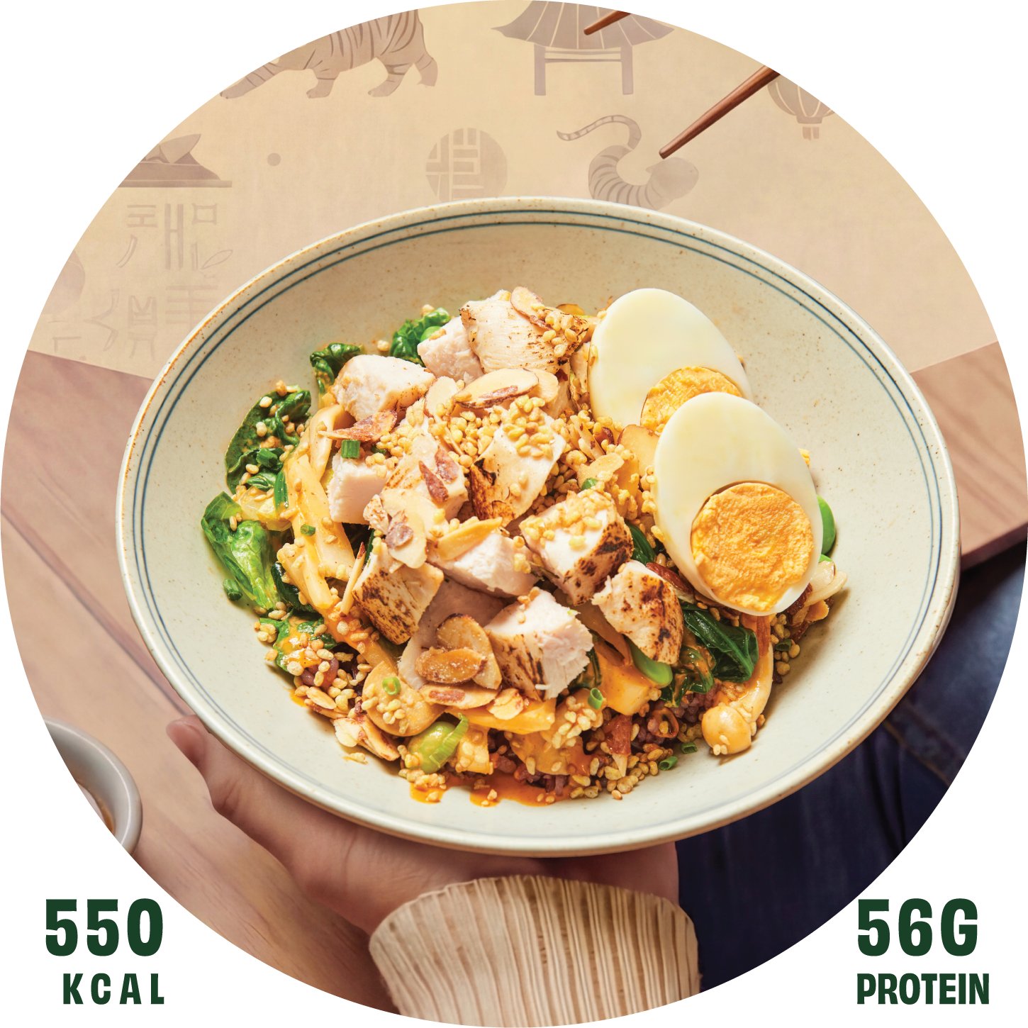 A bowl of grain bowl with chopped chicken, boiled eggs, vegetables, and crunchy toppings held in a person's hand over a wooden table.