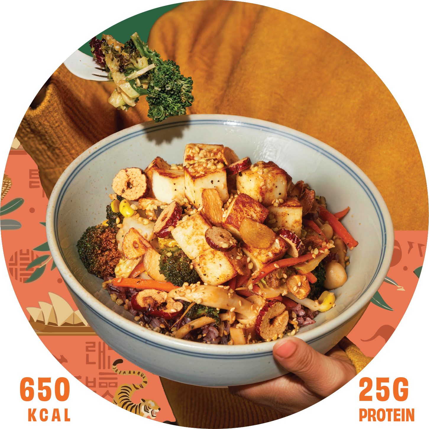 A hand holding a bowl of Asian-style tofu and vegetable stir-fry topped with sesame seeds, with a person's arm in a mustard-colored sweater visible in the background.