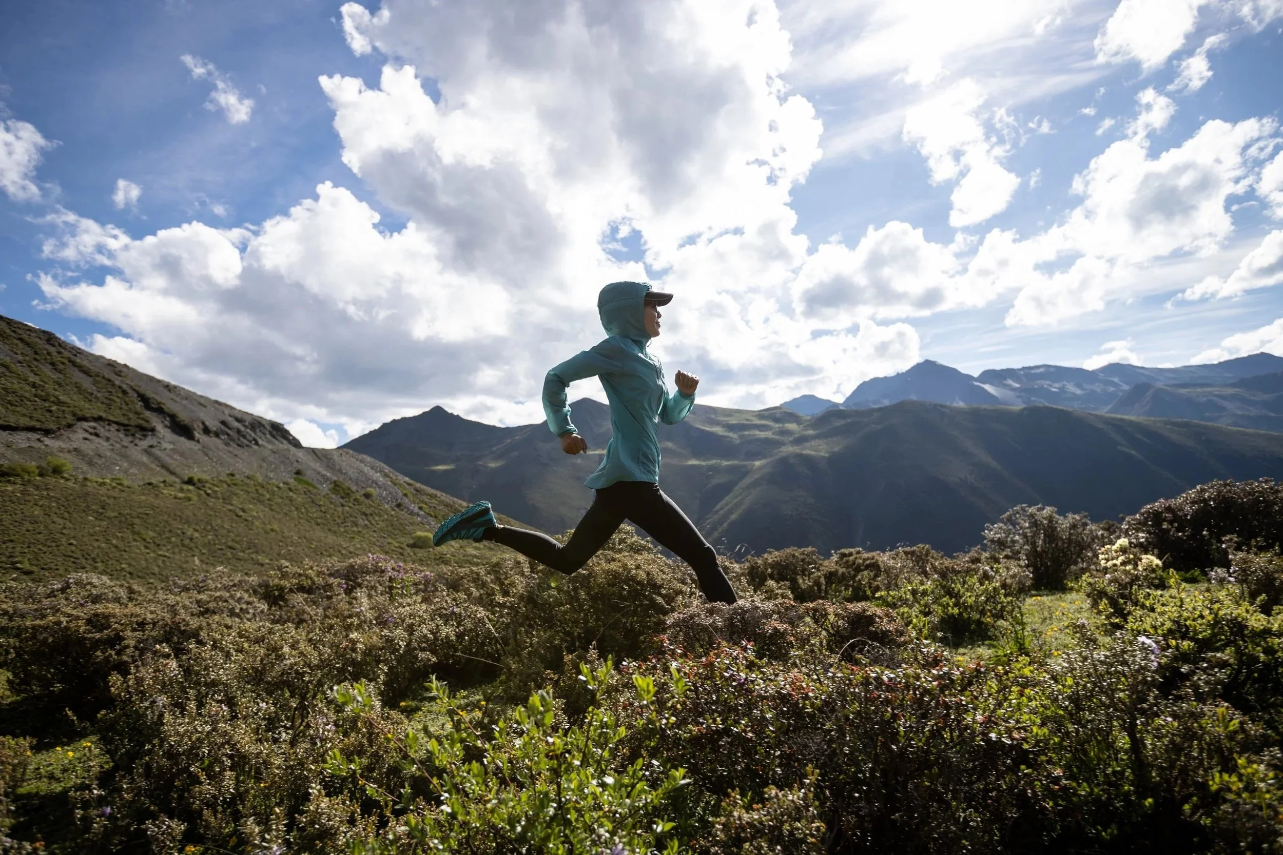 Person running outdoors in a mountainous landscape during daytime with a blue sky and white clouds. The image evokes wide horizons and a sense of freedom.