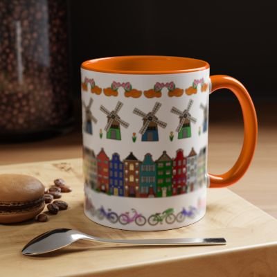 A ceramic mug with a colorful illustration of windmills, houses, and bicycles, placed on a wooden surface with coffee beans, a spoon, and a macaron nearby.