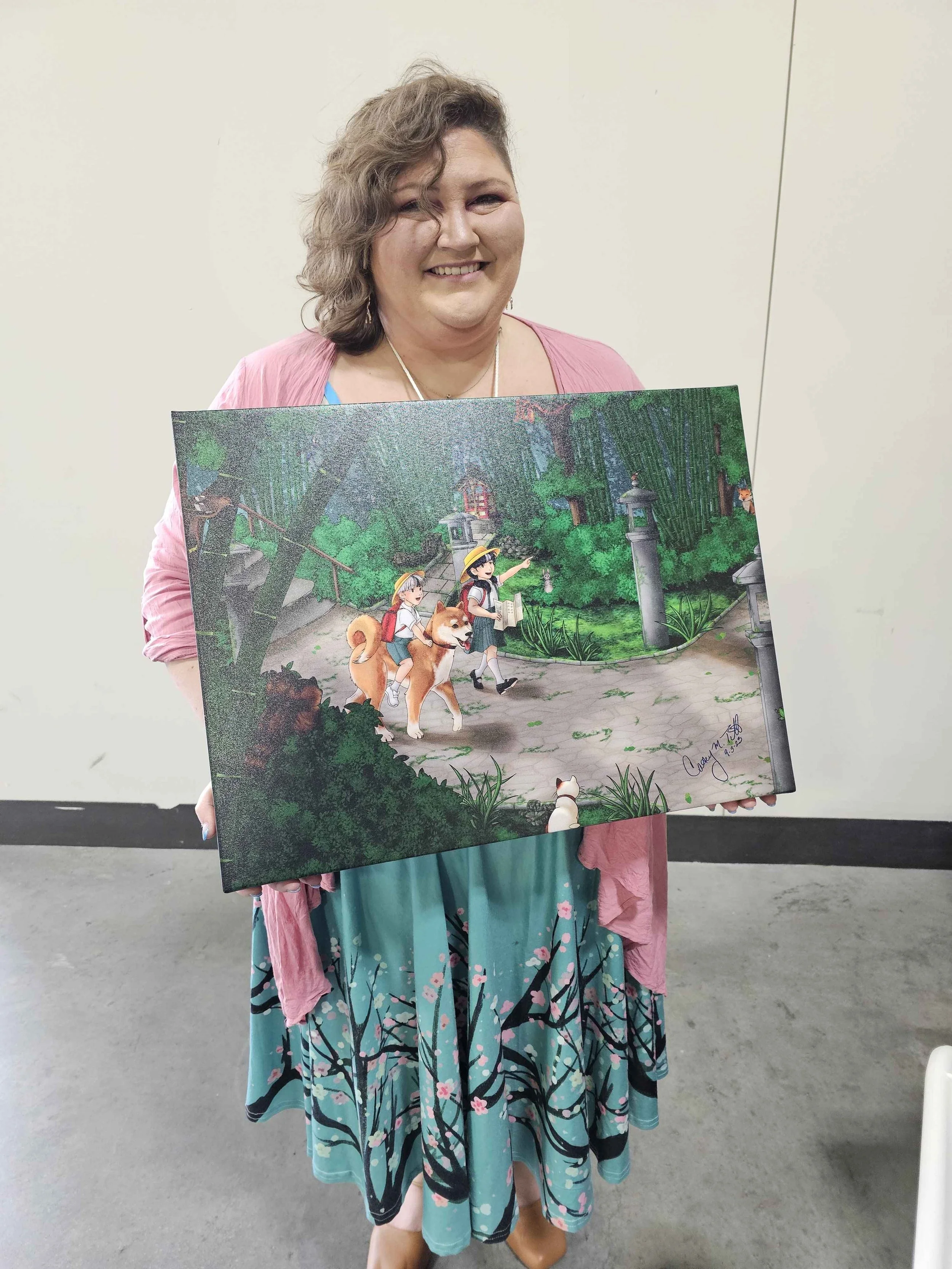 A woman holding a colorful painting of two children riding a dog through a lush forest path.