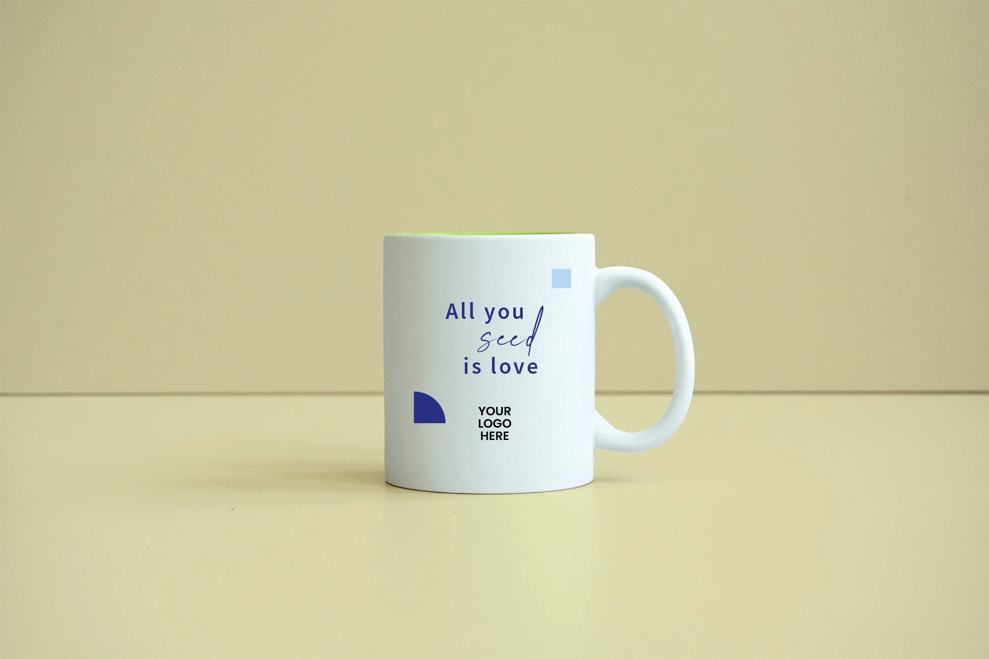 Taza blanca con texto en colores azul y negro que dice 'All you seed is love' y espacio para logo en la parte inferior, en un fondo color beige.