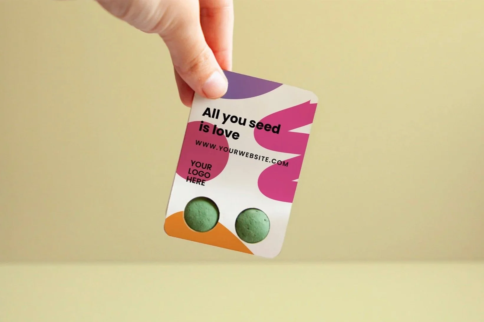 Persona sosteniendo una tarjeta con agujeros que muestran dos bolitas verdes, con texto en la tarjeta que dice 'All you seed is love' y un espacio para el logotipo.