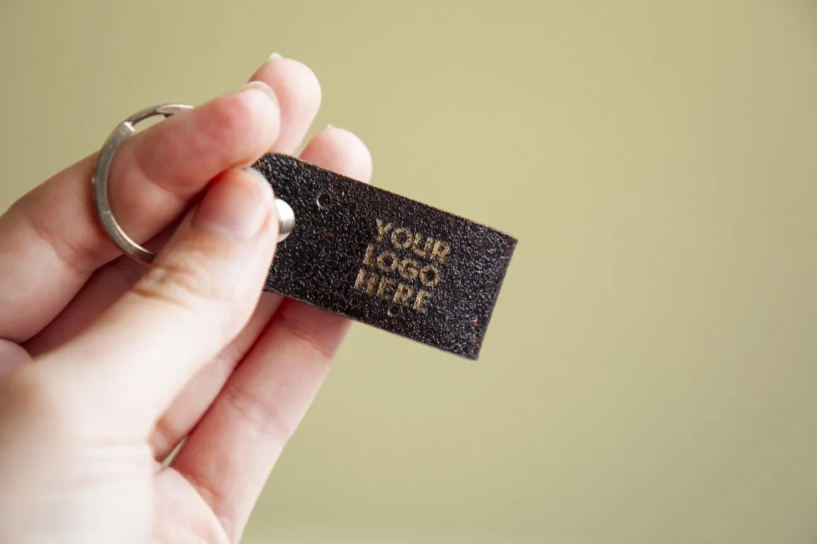 Llavero negro con la frase 'Your Logo Here' en letras doradas.
