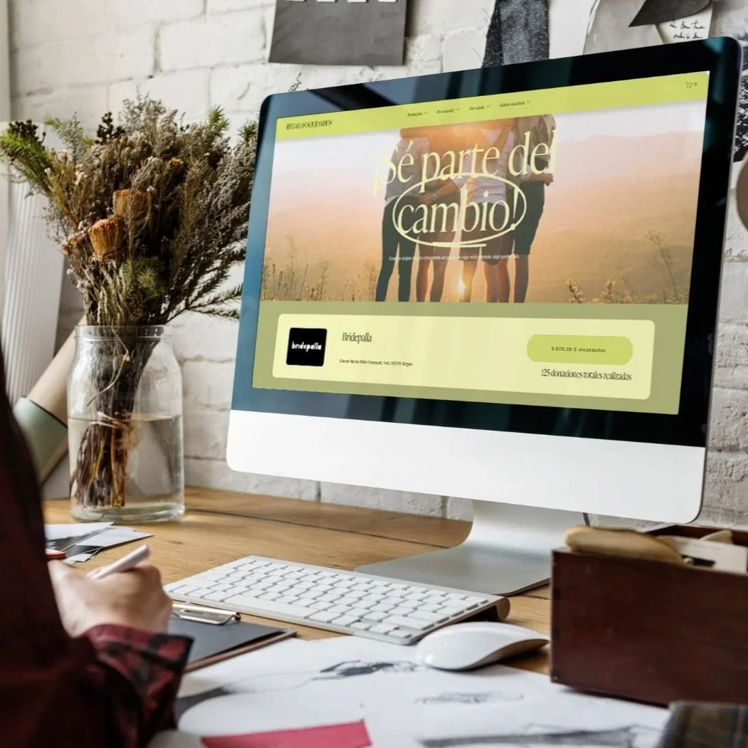 Pantalla de computadora con una página web que dice 'Sé parte de cambio!', en un escritorio rodeado de objetos de oficina y una jarra con flores secas al fondo.