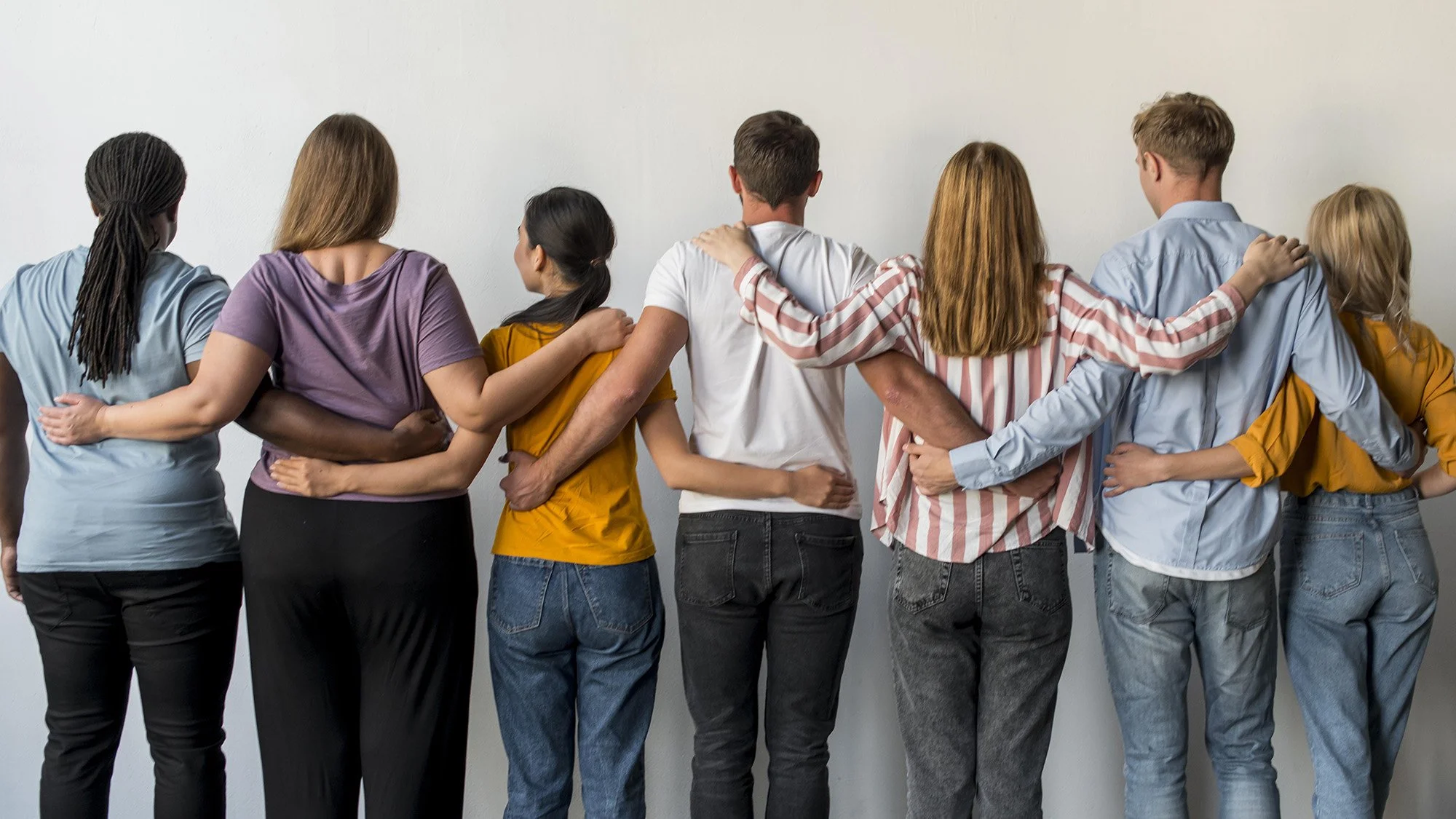 Grupo de personas de espaldas, con brazos alrededor de los hombros, formando una línea.