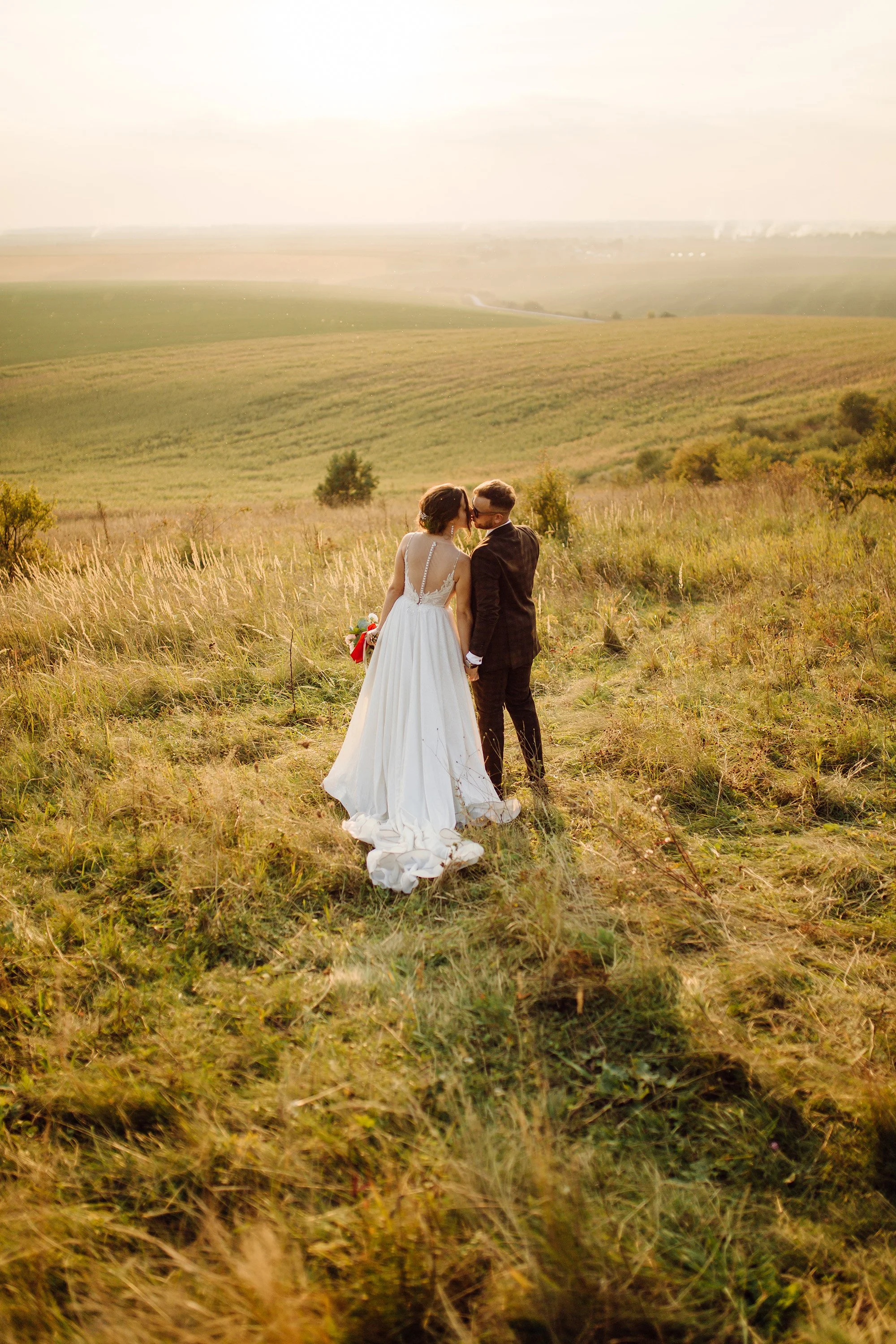 Una pareja de novios en un campo, en un momento romántico, en un paisaje de praderas y colinas bajo un cielo despejado.