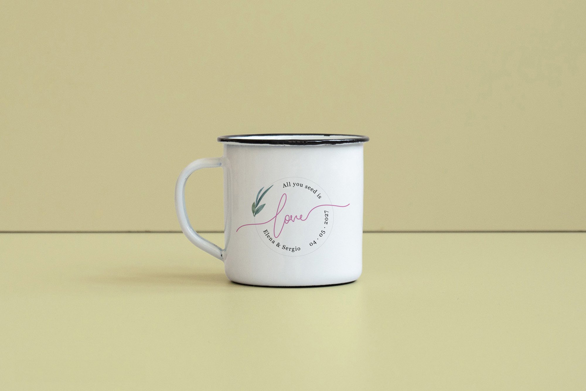 Taza blanca con borde negro, con texto y diseño de una hoja verde y rosa, en un fondo amarillo suave.