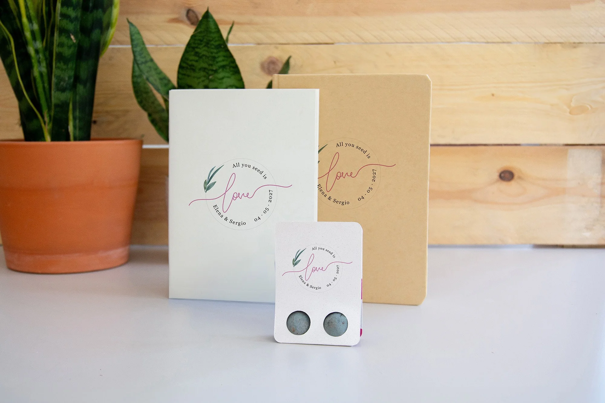 Varias libretas blancas y unakraft sobre una mesa blanca, en un fondo de pared de madera. Con diseño de bodas.