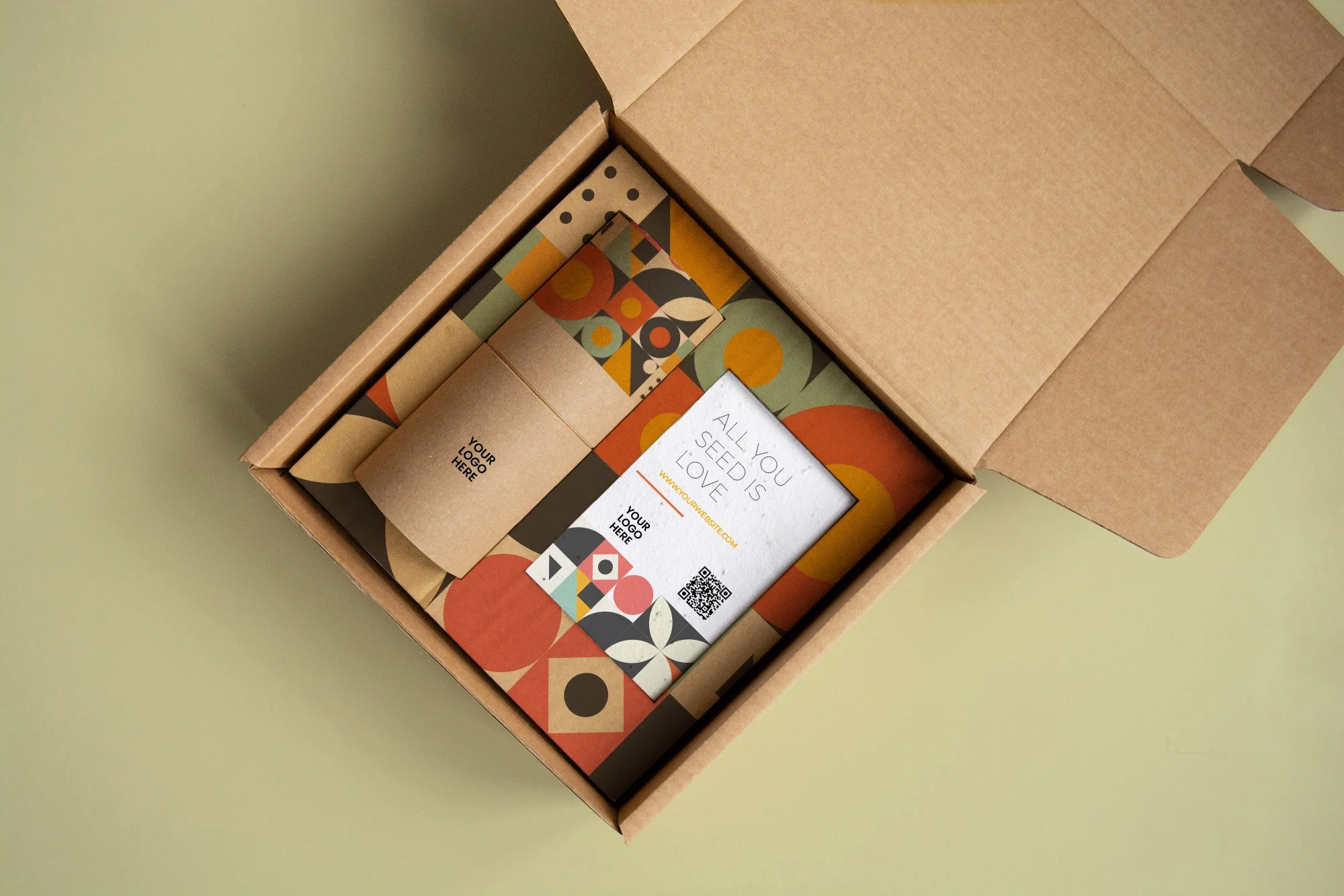 Caja de cartón abierta que contiene pequeños bloques de papel con diseños coloridos y un folleto que dice "All you seed is love" con el logo y detalles de contacto.