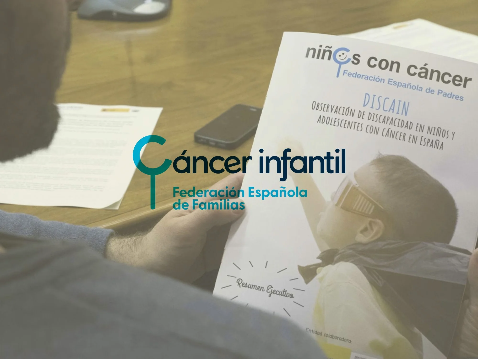 Documento con título 'niños con cáncer' del Federación Española de Padres, sobre observación de discapacidad en niños y adolescentes con cáncer en España, en una mesa de madera con móvil y hojas a su lado.