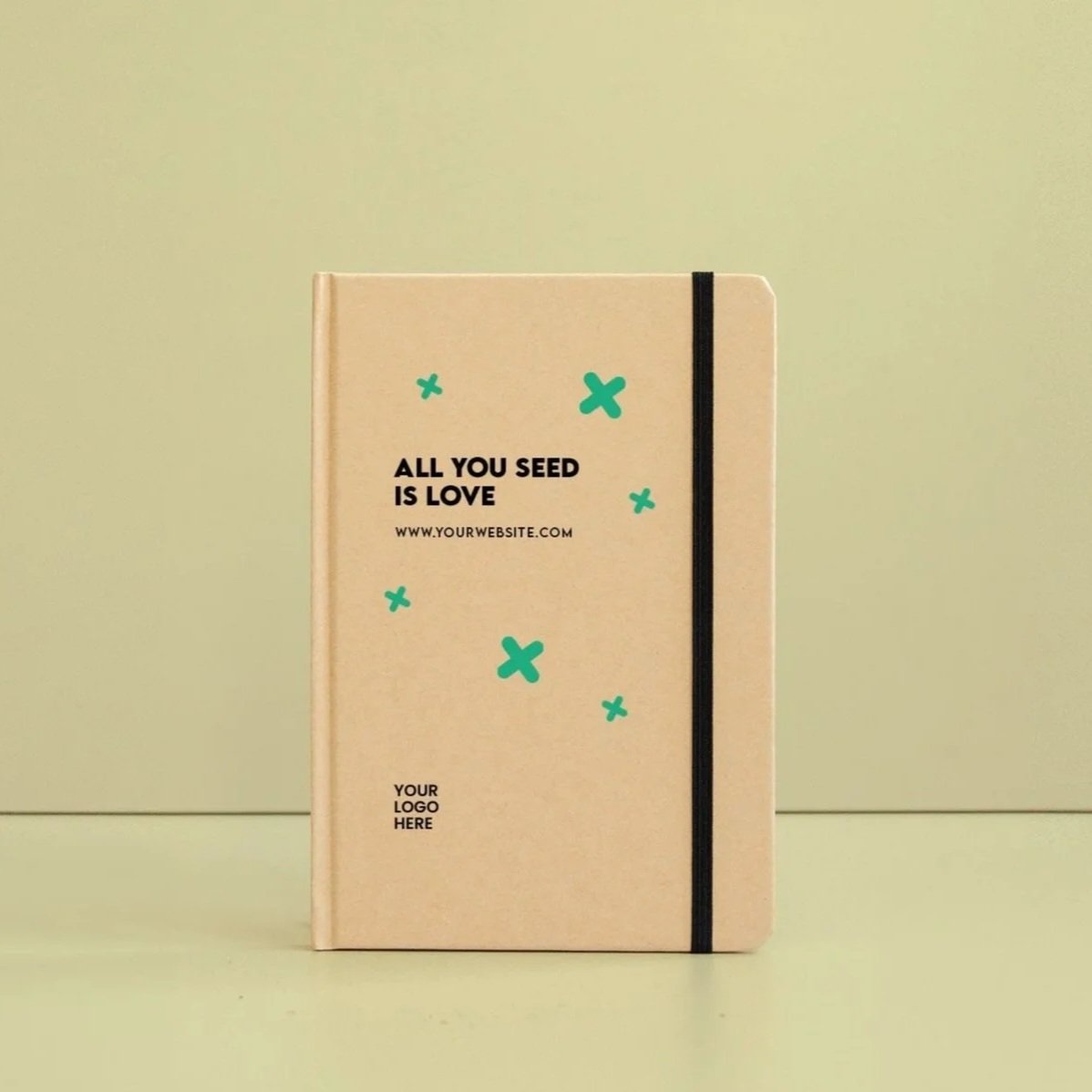 Cuaderno kraft con la frase "All you seed is love" en la portada, decorada con dibujos de cruces de color verde azulado, y una liga negra en el lado derecho. Un espacio para colocar un logotipo está en la parte inferior izquierda.