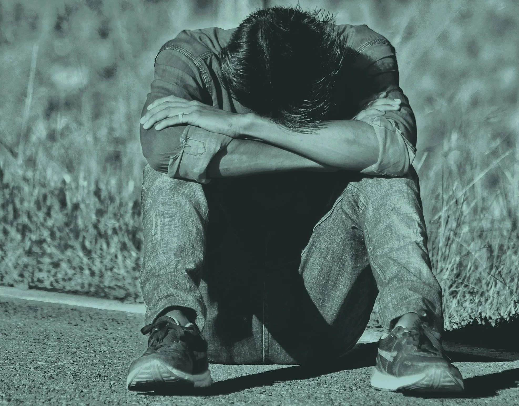 A person sitting on the ground with their head down and arms crossed over their knees, appearing distressed or upset.