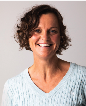 Smiling woman with short curly brown hair wearing a light blue sweater.