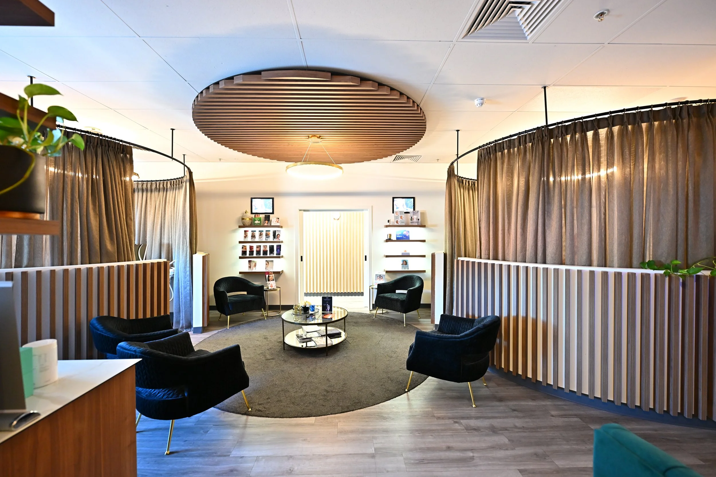 Interior of a modern office or waiting area with black chairs, a small round table, wood-paneled wall dividers, and a circular ceiling fixture.