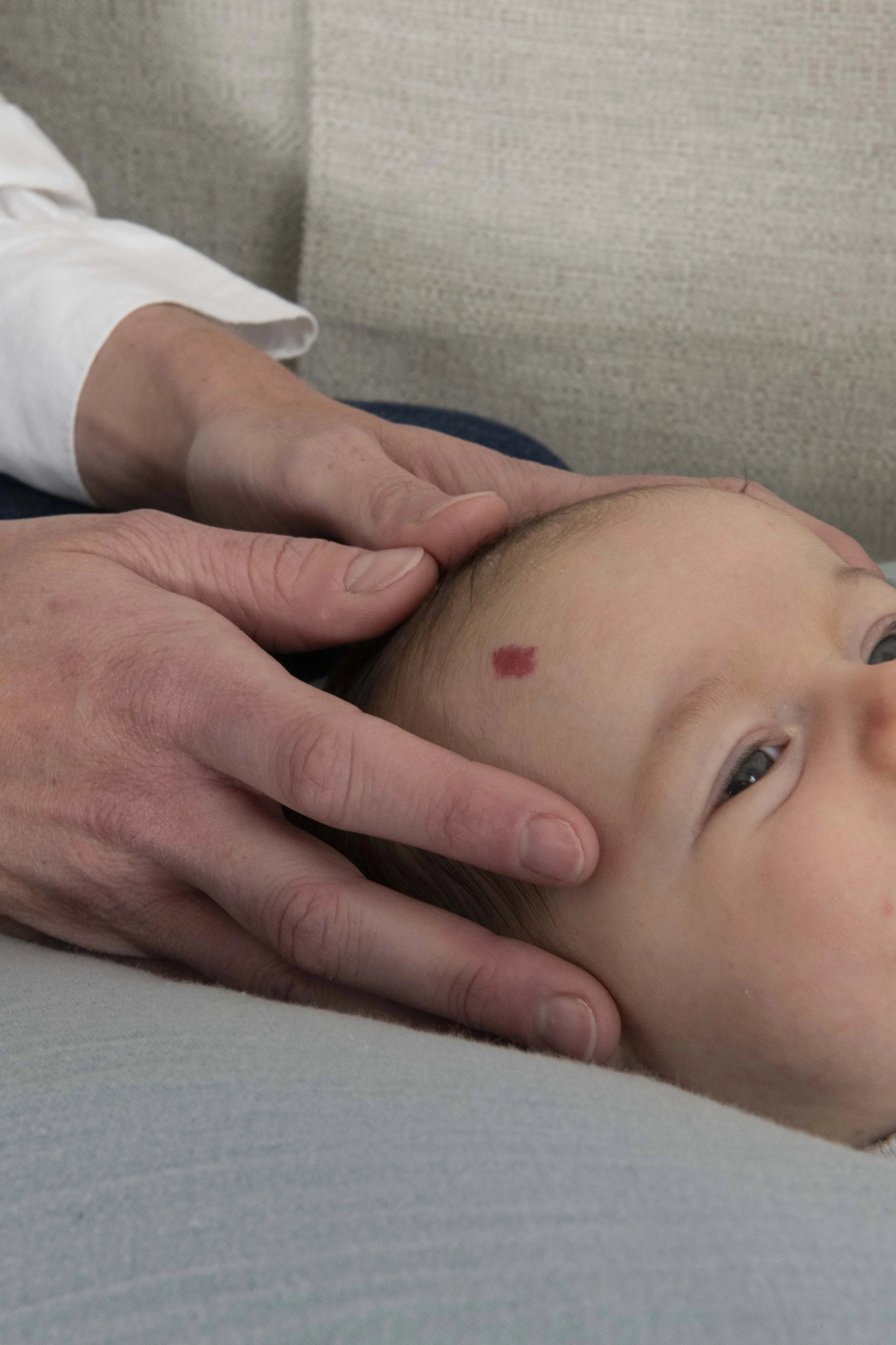 Un médecin ou un professionnel de la santé effectue une manipulation cervicale sur un enfant. L'enfant est allongé, visage tourné, avec une marque rouge sur le front.