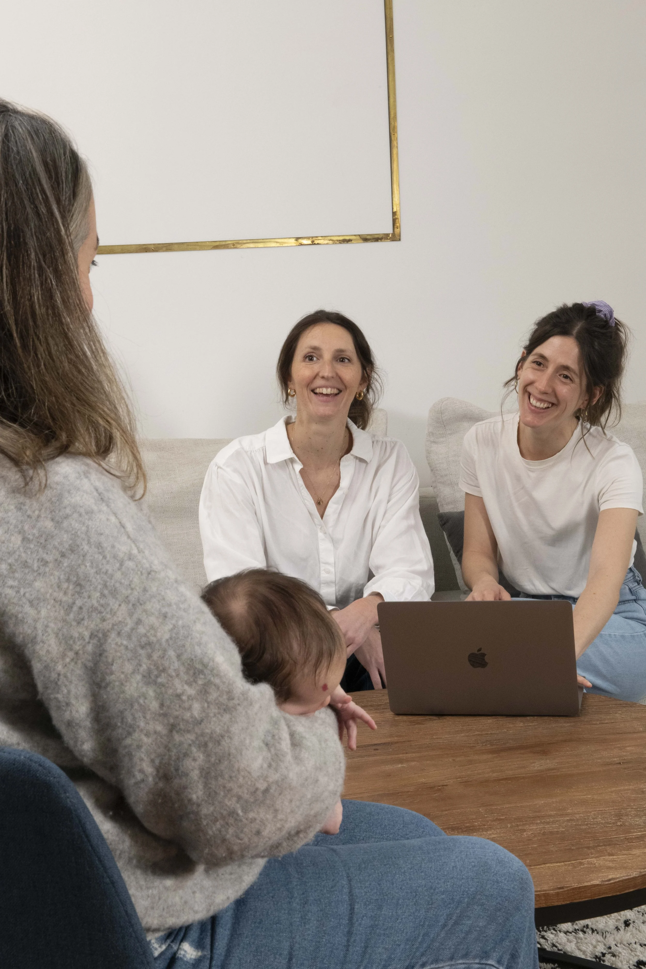 Trois femmes et deux enfants autour d'une table, en pleine discussion ou réunion, avec un ordinateur portable sur la table.