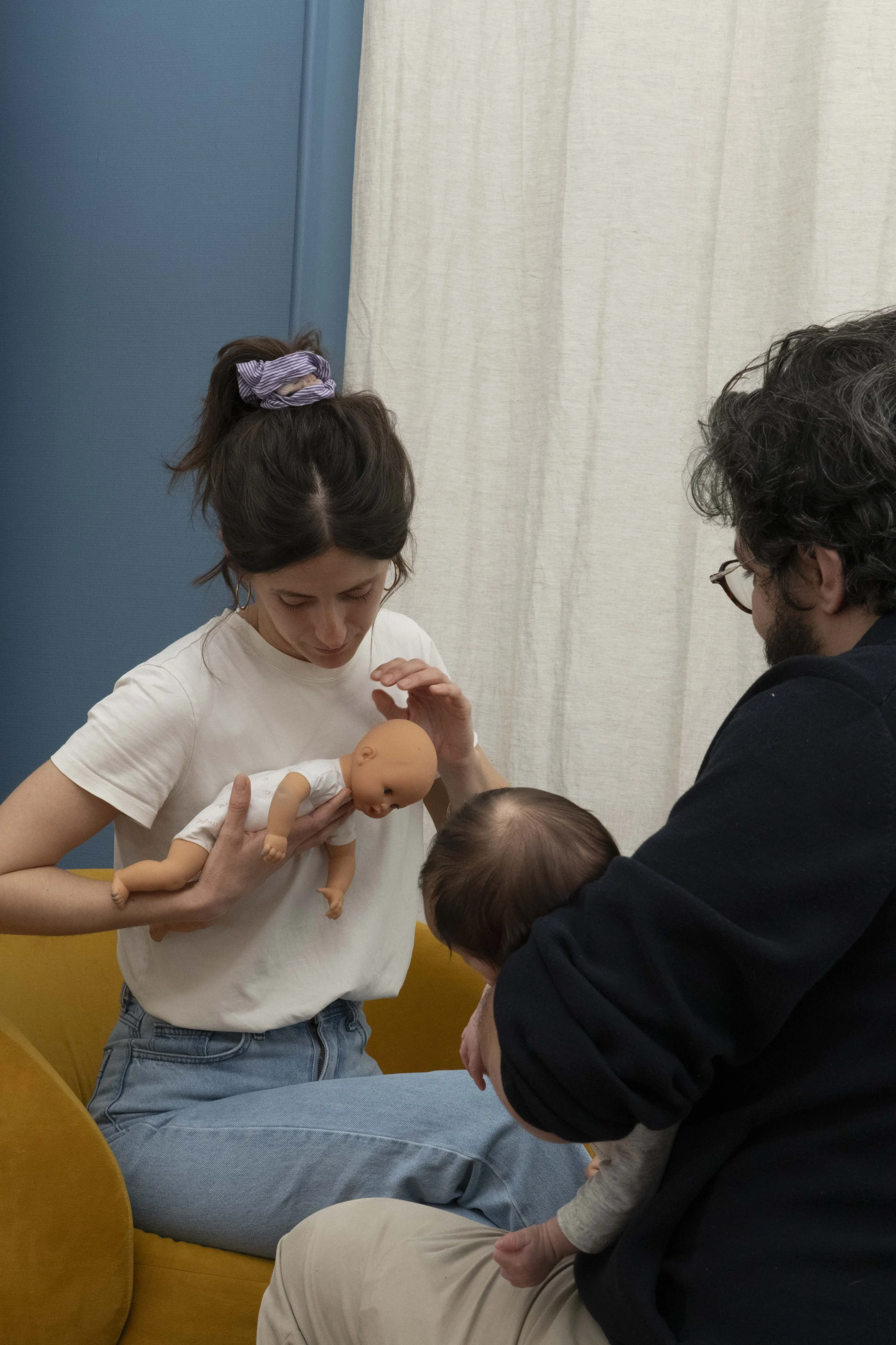 Un groupe de personnes, dont une femme tenant un bébé en plastique, participent à une activité éducative, probablement une séance d'instruction au sujet du secours ou des premiers soins.