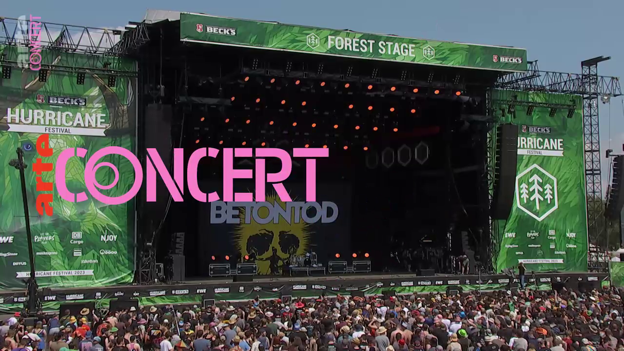 Large outdoor concert stage with green banners reading 'Hurricane Festival' and 'Forest Stage,' filled with a crowd of people attending.