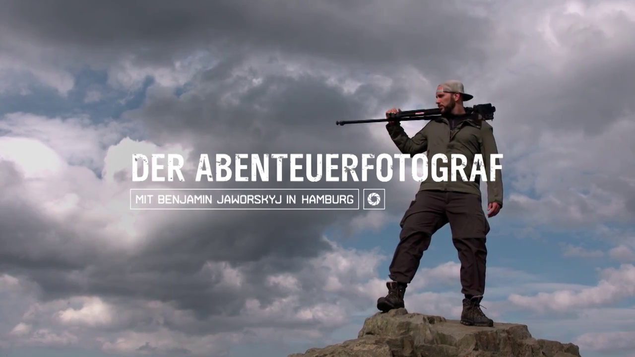 The photographer Benjamin Jaworskyj with a backpack and a camera tripod standing on a rocky outcrop, looking into the distance against a cloudy sky, with overlay text "Der Abenteuerfotograf"