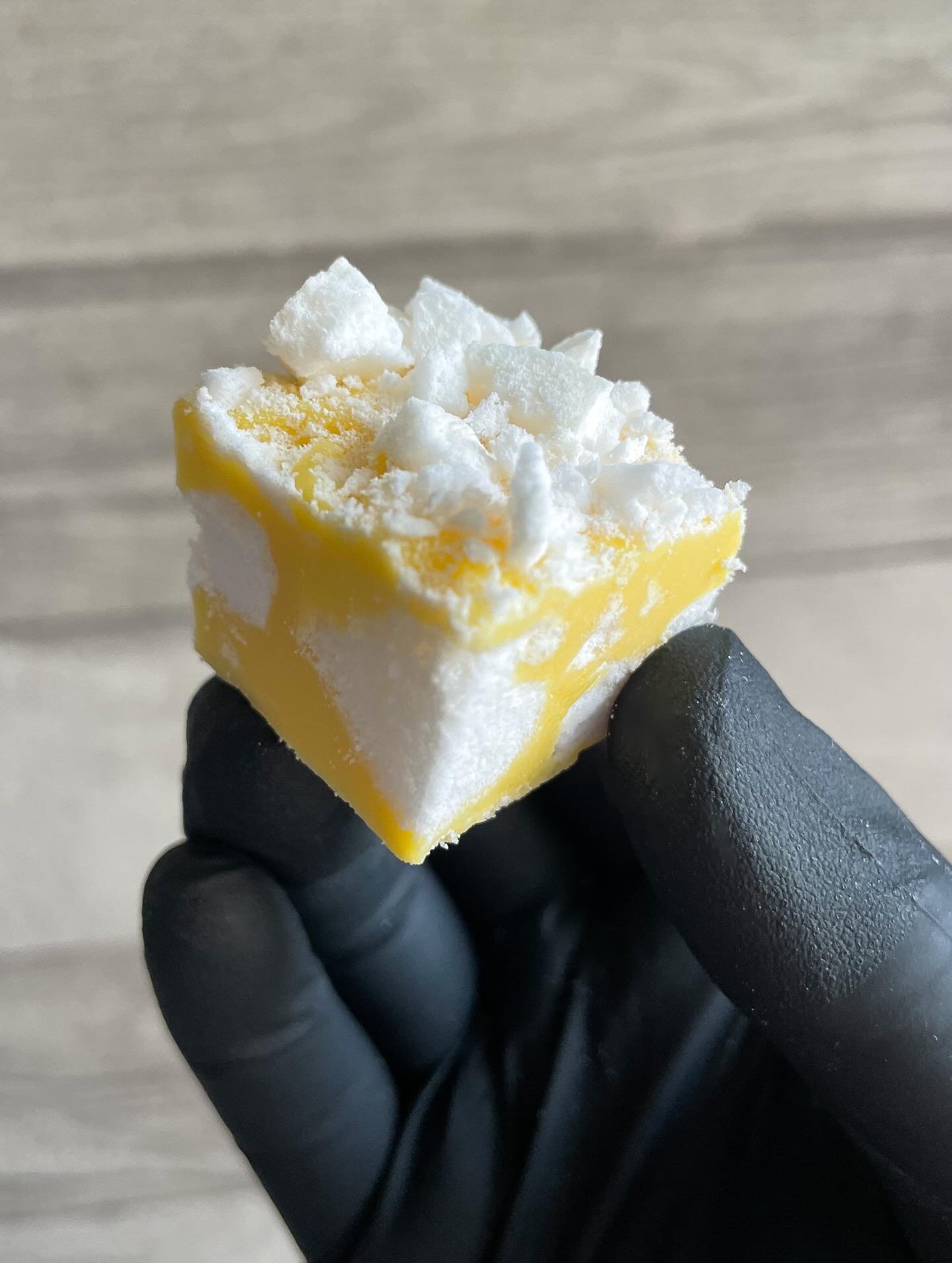 Close-up of a hand holding a yellow and white soap with white lather on top.