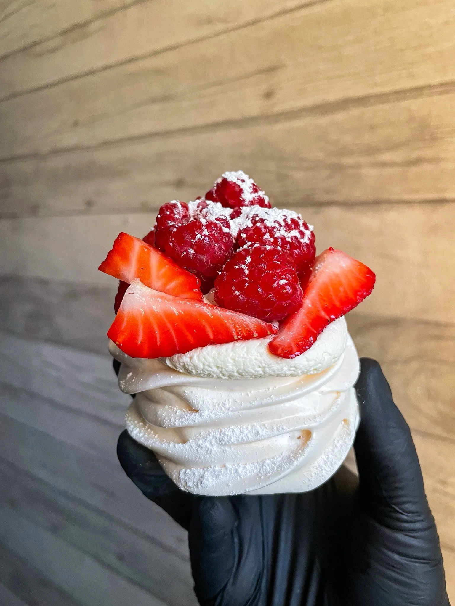 A dessert with whipped cream topped with sliced strawberries and raspberries sprinkled with powdered sugar, held in a black glove.