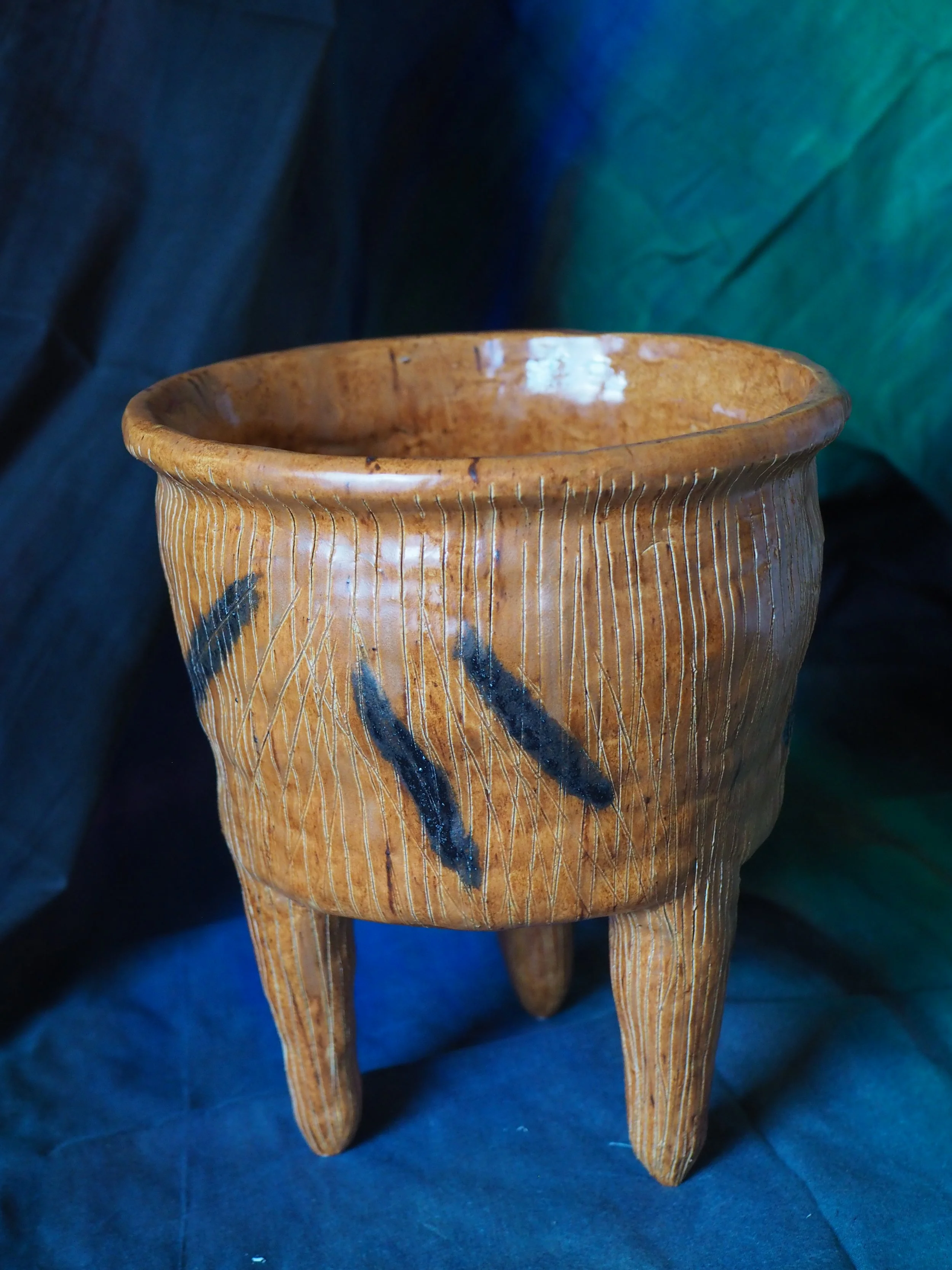 A wooden stool with carved details, including a black painted design, set against a dark background with fabric draping.