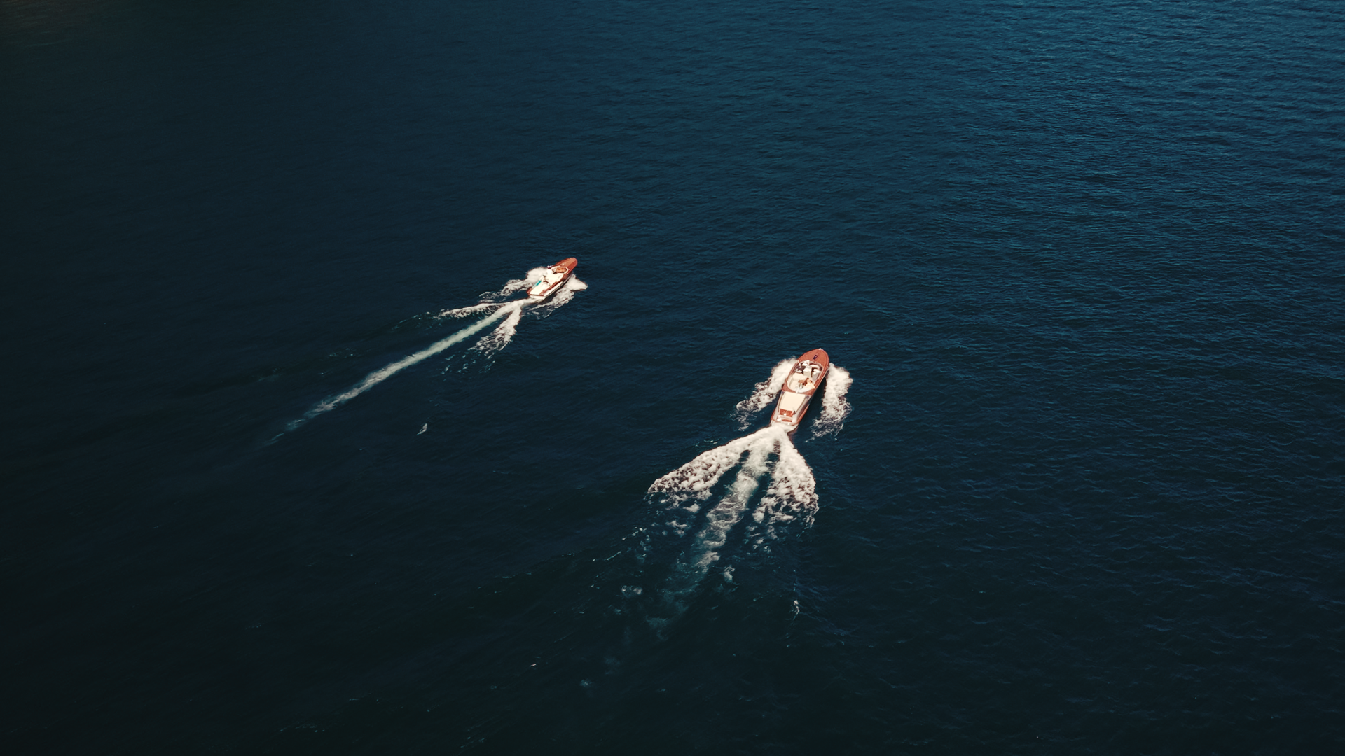 Two speed boats traveling across open water, creating white foam trails behind them.