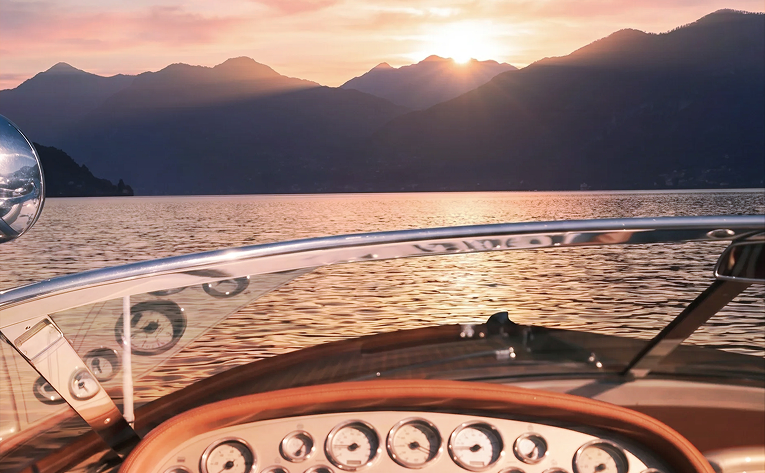 View from a boat dashboard overlooking a sunset over a mountain lake.