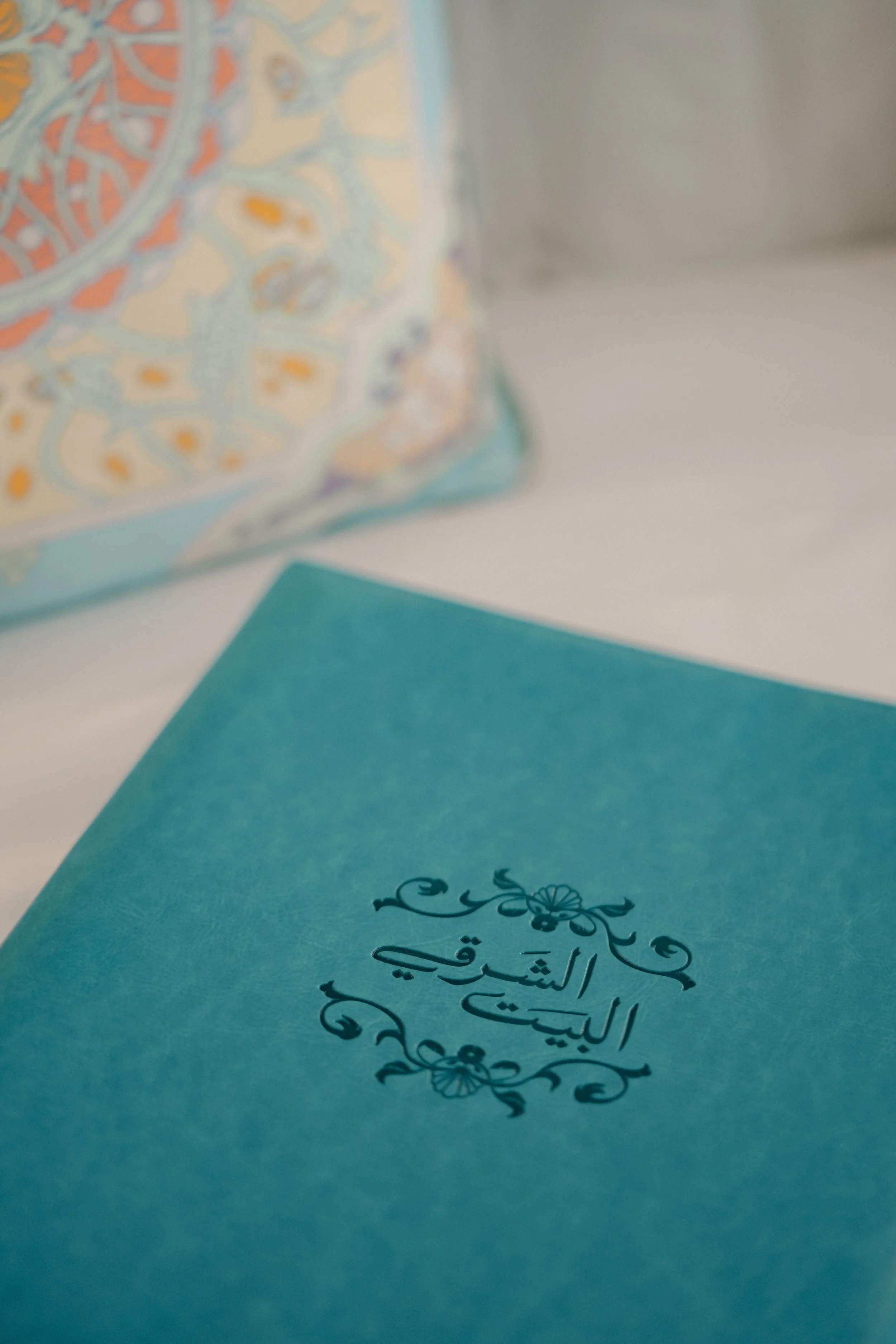 Close-up of a blue book with Arabic script and floral design on the cover, alongside a turquoise card with a decorative floral motif.